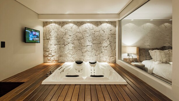 A modern bathroom with a stone wall, a large mirror, and a wooden floor. - Varanda Boutique Hotel (Gramado)