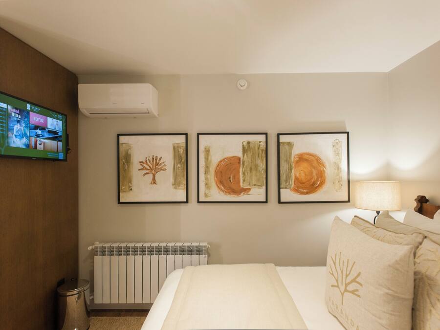 A hotel room with a bed, a TV mounted on the wall, and three framed artworks above the bed.