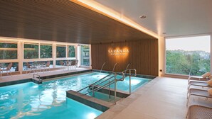 A modern indoor swimming pool with clear glass walls, a wooden ceiling, and a view of greenery outside. - Varanda Boutique Hotel (Gramado)