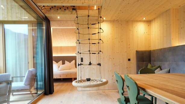 Un interior moderno con techo de madera, una escalera de cuerda colgante, una mesa de comedor con sillas y una cama con almohadas.