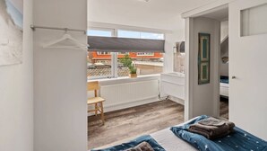 Una camera da letto con un letto, una finestra, un termosifone, una sedia e vista sugli edifici esterni.