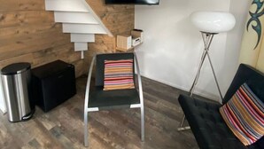Un soggiorno moderno con una scala in legno, una televisione a schermo piatto montata a parete, un divano nero con un cuscino a righe e un tavolino con un cuscino colorato a righe.