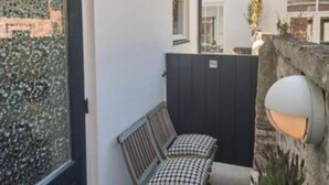 Una piccola zona esterna con due sedie e un tavolo, una lampada decorativa a parete e una pianta in vaso.