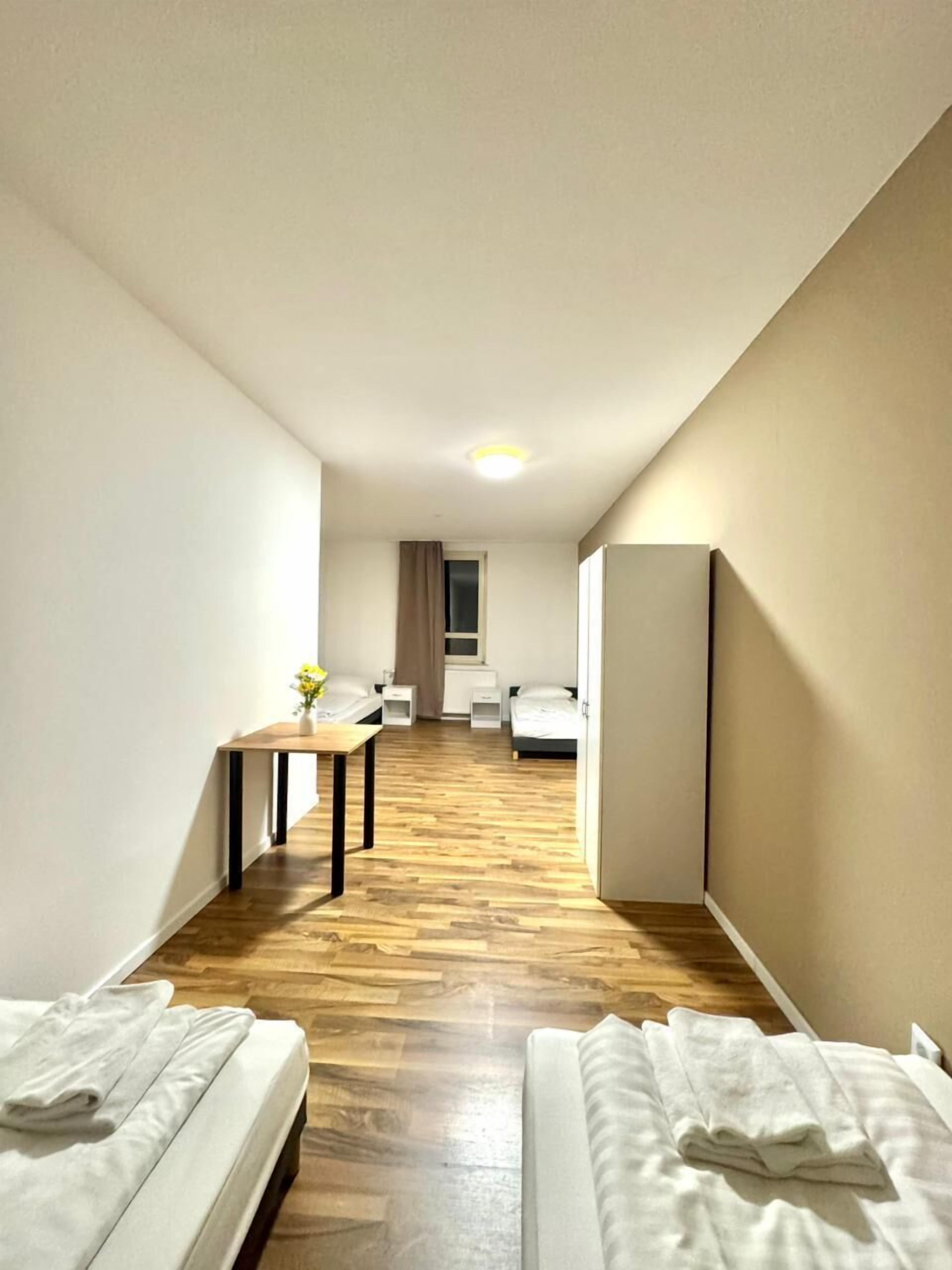 Une chambre d’hôtel avec deux lits, une petite table ornée d’un vase de fleurs, un bureau et une armoire.