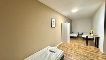 A compact room with a single bed, a small table with a vase, and a door leading to another room.
