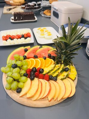 Een fruitschaal met druiven, aardbeien, blauwe bessen, ananas en appelpartjes op een houten plank.