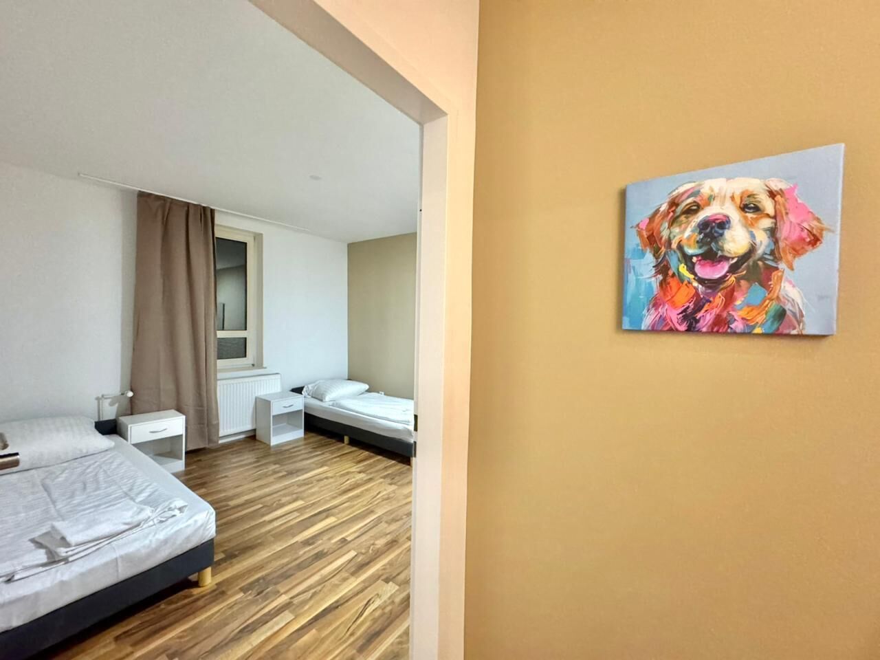 Una habitación de hotel moderna con suelo de madera, una cama, un escritorio y un ventanal con cortinas.