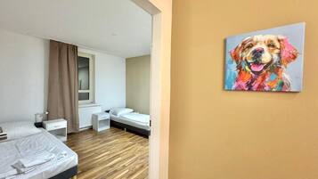 Una habitación de hotel moderna con suelo de madera, una cama, un escritorio y un ventanal con cortinas.