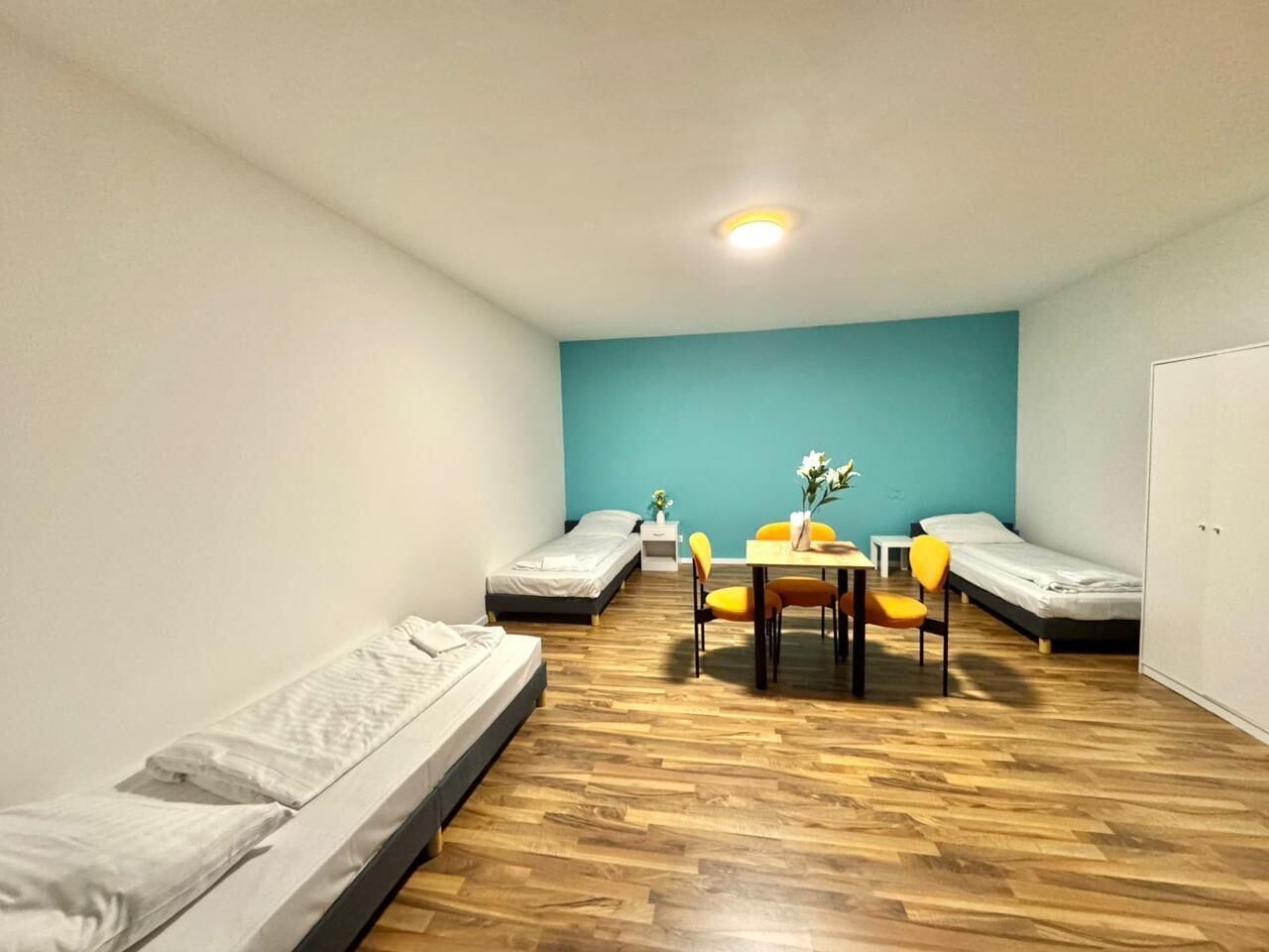 Una habitación con dos camas individuales, una mesita con sillas y una pared de acento color verde azulado.