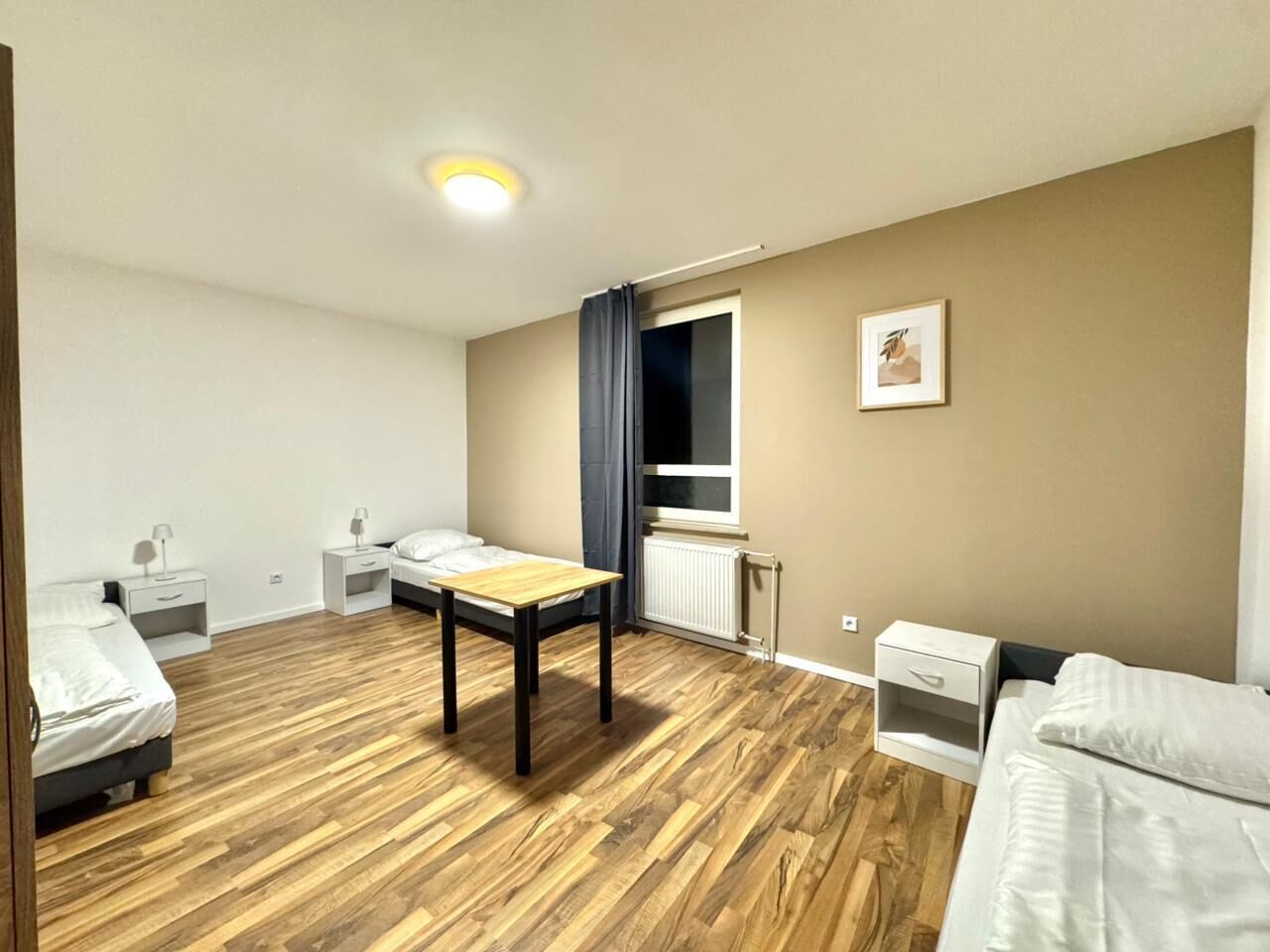 Une chambre avec deux lits, un plancher en bois, une table et une fenêtre avec des rideaux.