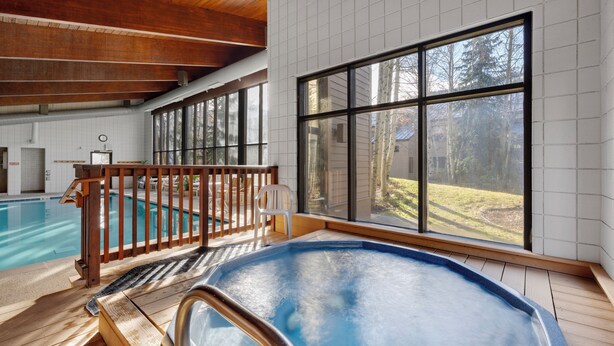 An indoor swimming pool with a wooden deck, large windows, and a view of the outdoors.