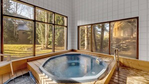 A hot tub in a room with large windows, wooden flooring, and a view of a yard.