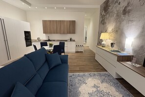 Un salon moderne avec un canapé bleu, une cuisine en arrière-plan et un grand tableau abstrait accroché au mur.