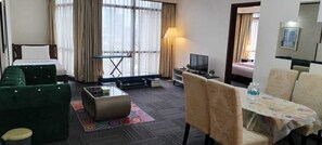 A hotel room with a bed, a green sofa, a coffee table, a TV, a dining table with chairs, and a large window with curtains. - BEJAYA TIMES SQUARE SERVICE APARTMENT  (Kuala Lumpur)