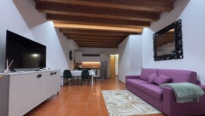 A compact living space with a dining area, a sofa, a TV, and a kitchen in the background. - Veronetta 52 Garden - Verona Journeys (Verona)