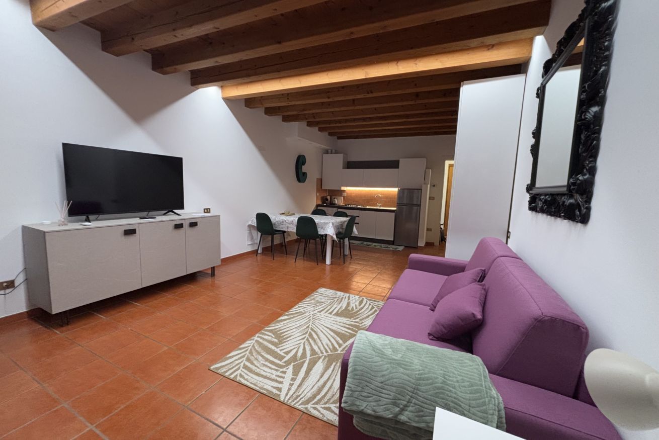Een woonkamer met een televisie, bank en een eethoek met stoelen en een tafel.