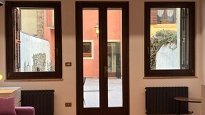 A room with a double door, two windows, a radiator, and a small table. - Veronetta 52 Garden - Verona Journeys (Verona)