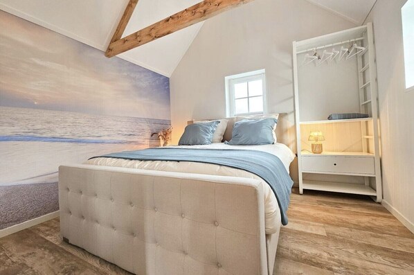 A bedroom with a large bed, a nightstand, a wardrobe, and a mural of a beach scene.