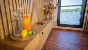 A wooden counter with a view of a body of water, a vase with dried plants, and a tray with a lemon and a bottle. - Floatinghouse Aquila WOMA D13 – Modern Houseboat for 6 Guests with Rooftop Terrace (Fürstenberg)