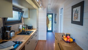 A modern kitchen with a stove, sink, and window, leading to a hallway with a door and framed artwork. - Floatinghouse Aquila WOMA D13 – Modern Houseboat for 6 Guests with Rooftop Terrace (Fürstenberg)