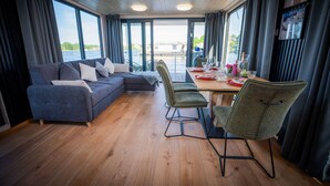 A modern interior with a sofa, chairs, a dining table, and large windows offering a view of the water.