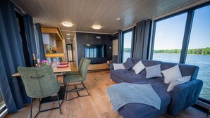 A modern interior with a dining area, a sofa, and a large window overlooking a body of water.