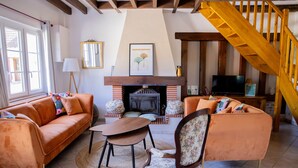 Un salon avec une cheminée, un canapé, un fauteuil, un escalier en bois et un téléviseur.