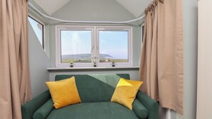 Una habitación con un sofá verde, cortinas color beige y una ventana que ofrece vistas a un paisaje.
