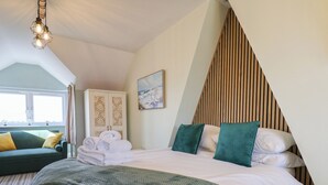 Un dormitorio con una cama, un sofá verde, techo inclinado de madera y un cuadro en la pared.