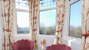 Una habitación con dos sillones rosa, una mesita redonda con un florero y una ventana con cortinas estampadas.