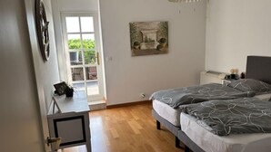 Makuuhuoneessa on sänky, yöpöytä, lamppu ja ovi, joka johtaa ulkotilaan, jossa on kasveja.