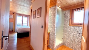 Ein Holzboden-Flur führt zu einem Schlafzimmer mit Bett und Stuhl, sowie zu einem Badezimmer mit Mosaikwand und Fenster.