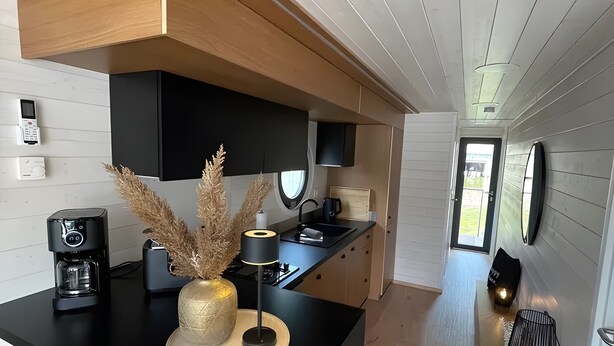 A modern kitchen with a central island, built-in appliances, and a flat-screen TV. - Floatinghouse Enjoy WOMA D13 – Modernes Hausboot mit Dachterrasse am Röblinsee (Fürstenberg)