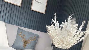 A modern living room with a grey sofa, a decorative sculpture, a tall vase with white foliage, and a framed artwork on the wall. - Floatinghouse Enjoy WOMA D13 – Modernes Hausboot mit Dachterrasse am Röblinsee (Fürstenberg)