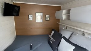 A compact room with a bed, a mounted TV, and a wooden headboard. - Floatinghouse Enjoy WOMA D13 – Modernes Hausboot mit Dachterrasse am Röblinsee (Fürstenberg)