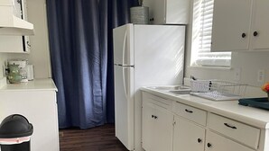 Eine kleine Küche mit weißen Schränken, einem Kühlschrank, einer Mikrowelle und einem Mülleimer.