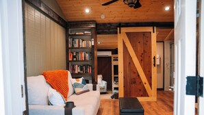 Ein gemütliches Wohnzimmer mit einer Couch, einem Bücherregal, einer Holztür und einem Deckenventilator.