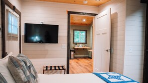 Ein Schlafzimmer mit einem Bett, einem an der Wand befestigten Fernseher und einer Holzbalkendecke.