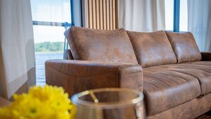 A brown leather sofa with a view of the water outside. - Floatinghouse Frigga WOMA D13 – Modernes Hausboot mit Dachterrasse am Röblinsee (Fürstenberg)
