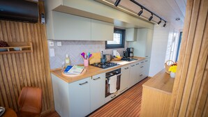 A compact kitchen with a wooden countertop, a gas stove, a sink, and a window. - Floatinghouse Frigga WOMA D13 – Modernes Hausboot mit Dachterrasse am Röblinsee (Fürstenberg)