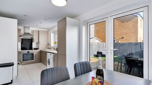 Een moderne keuken met een inbouwoven, een wasmachine en een eethoek met een tafel en stoelen.