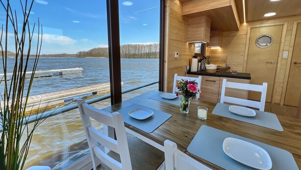 Comedor con vista al agua, paredes de madera y una cocina moderna.