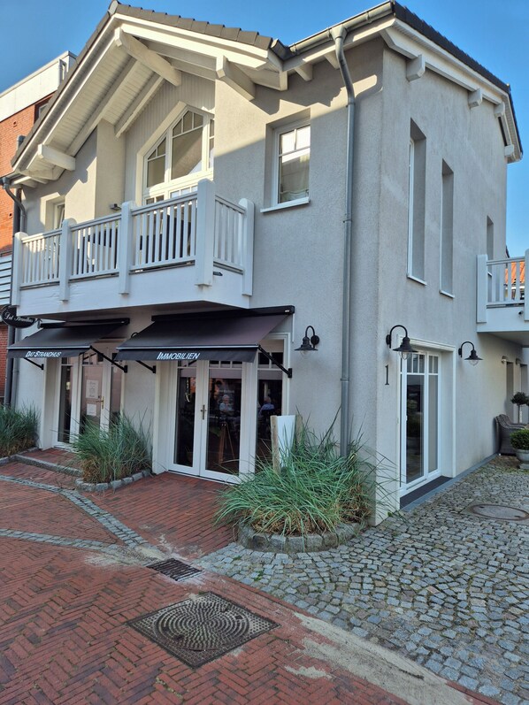A two-story building with a balcony, a ground-level entrance with a black awning, and a cobblestone driveway. - Apart Pier 2 ***** Vacation Rental in a Prime Location (Büsum)