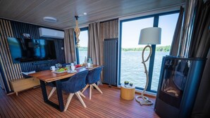 Un interior moderno con piso de madera, una mesa de comedor con sillas, un televisor y un ventanal con vista al agua.