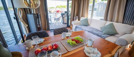 A dining area with a wooden table, chairs, a sofa, and a view of the water outside.