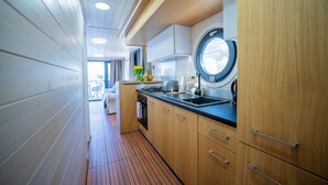 Un estrecho pasillo con paredes y suelo de madera, una zona de cocina con estufa, lavabo y armarios, y una ventana con vistas.