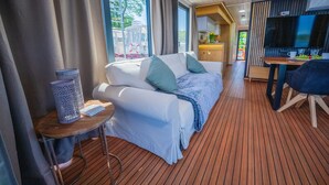 Una habitación moderna con cama, una mesa con lámpara, televisor y una zona de cocina.
