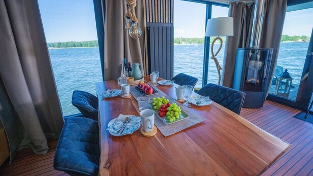 Un comedor con una mesa de madera, sillas tapizadas en azul y vista al agua.