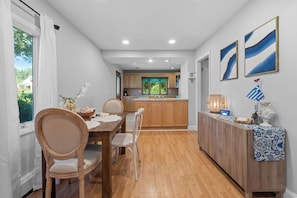 A modern kitchen with wooden cabinets, a dining table with chairs, and a view to the outside.