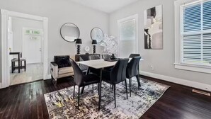 A modern dining room with a white table and black chairs, a black and white rug, and a large window with blinds. - Petersburg Vacation Gem 3BR - Private Backyard (Petersburg)
